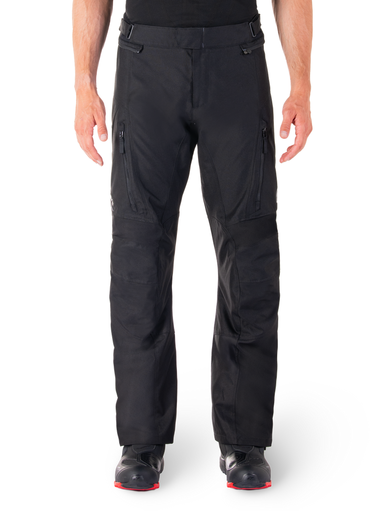 Alpinestars ST-1 Waterproof Pants, Black Motorcycle Touring Pants, front view featuring vertical zippered thigh pockets and adjustable waist tabs, worn with black red-soled boots, plain white background
