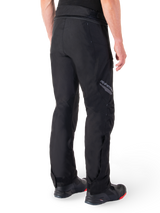 Alpinestars St-1 Waterproof Pants, Black, rear view showing textile construction and Alpinestars branding on the thigh, worn with black motorcycle boots, adventure touring style