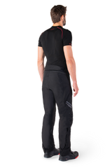 Alpinestars St-1 Waterproof Pants, Black motorcycle touring pants, three-quarter rear view on a model wearing a black base layer and black riding boots, featuring reflective Alpinestars branding on the thigh and a streamlined ergonomic design.
