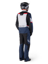Rear view of a motorcycle rider wearing Alpinestars ST-1 Waterproof Pants and matching jacket in Dark Blue Black and Bright Red, adventure touring gear with textile panels and reflective accents, paired with a black helmet and boots.