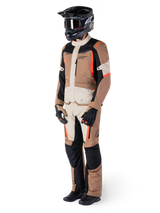 Rider wearing Alpinestars ST-1 Waterproof adventure touring suit, Dark Khaki Sand and Black jacket and pants with Red Fluo accents, black helmet and gloves, showcasing a complete waterproof outfit for all-weather motorcycle riding