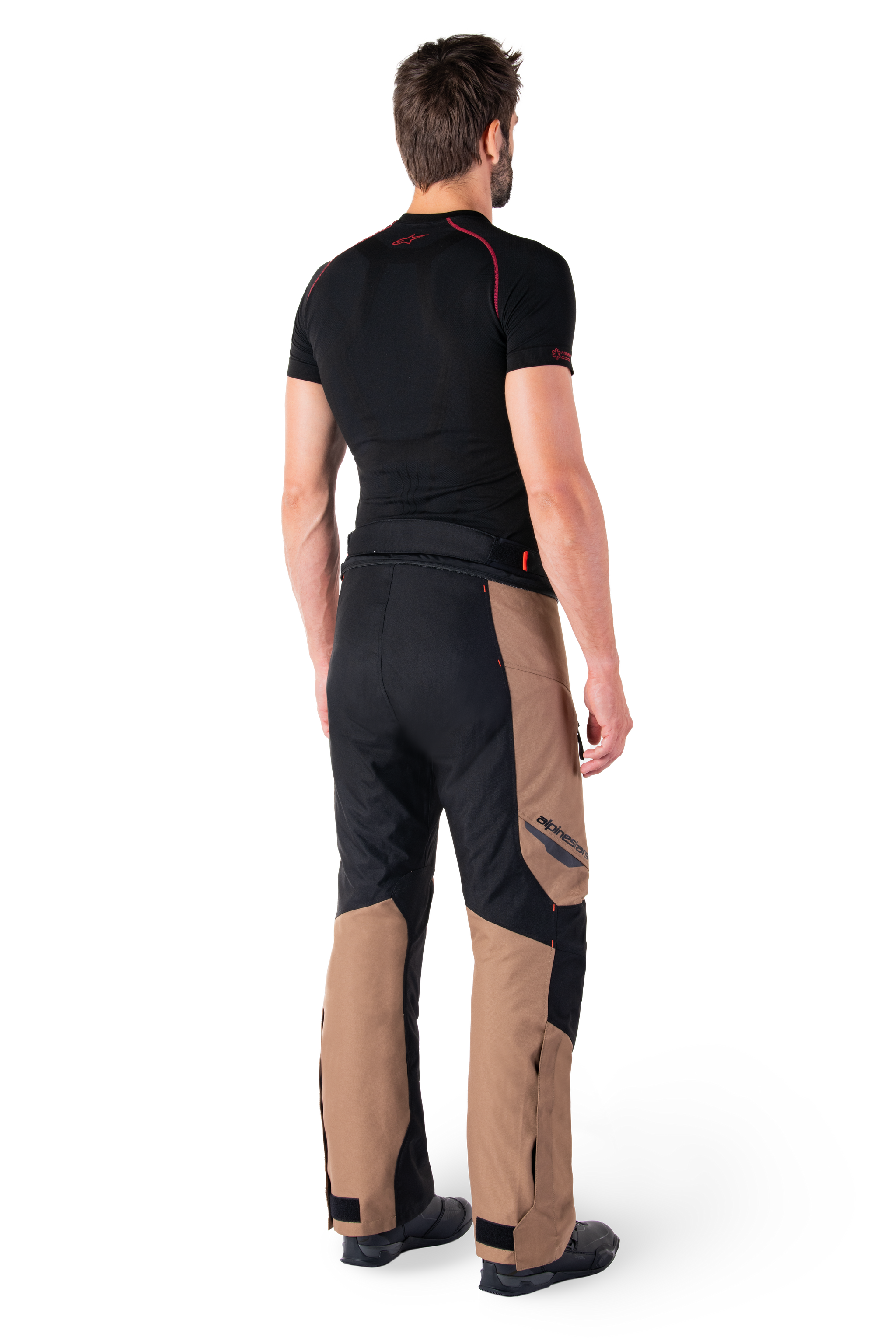 Alpinestars St-1 Waterproof Pants, motorcycle touring pants, Dark Khaki Sand and Black with Red Fluo accents, rear view on a model, featuring durable textile panels, Alpinestars logo on the thigh, and adjustable ankle cuffs, designed for all-weather adventure riding.