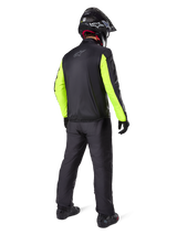 Rider from the rear wearing Alpinestars Bogotá Pro Drystar® 3 Seasons Pants in Black, paired with a black jacket featuring fluorescent yellow sleeves, black adventure helmet, and boots, complete adventure touring gear
