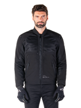 Alpinestars Mootant Waterproof Parka, Black motorcycle jacket, Front view on male model, featuring modular textile construction with mesh panels for ventilation, ribbed collar, and zippered pockets, worn with black gloves with white Alpinestars branding