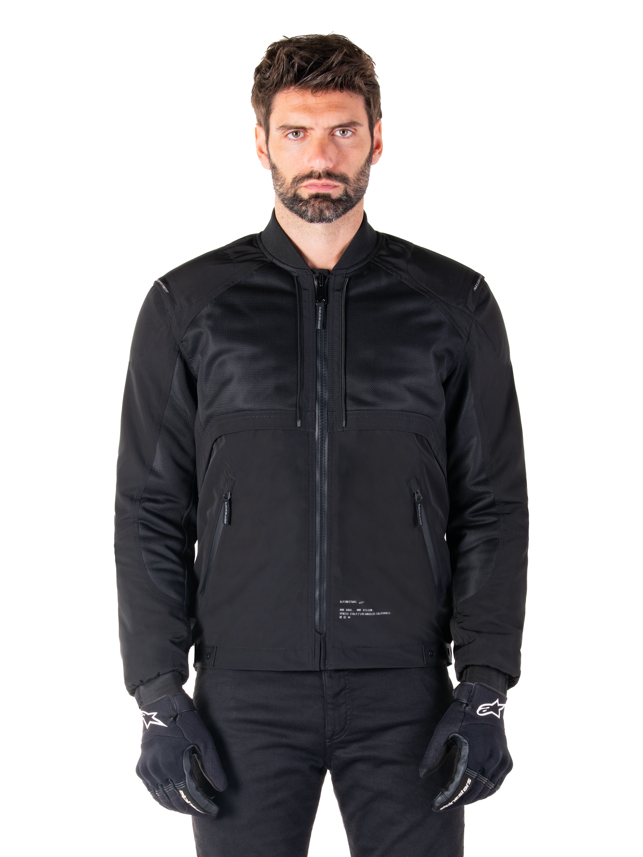 Alpinestars Mootant Waterproof Parka, Black motorcycle jacket, Front view on male model, featuring modular textile construction with mesh panels for ventilation, ribbed collar, and zippered pockets, worn with black gloves with white Alpinestars branding