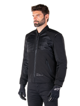 Alpinestars Mootant Waterproof Parka, modular black motorcycle jacket shown in its bomber configuration with mesh upper body panels and a ribbed collar, worn by a model with black riding gloves and pants, urban contemporary streetwear style.