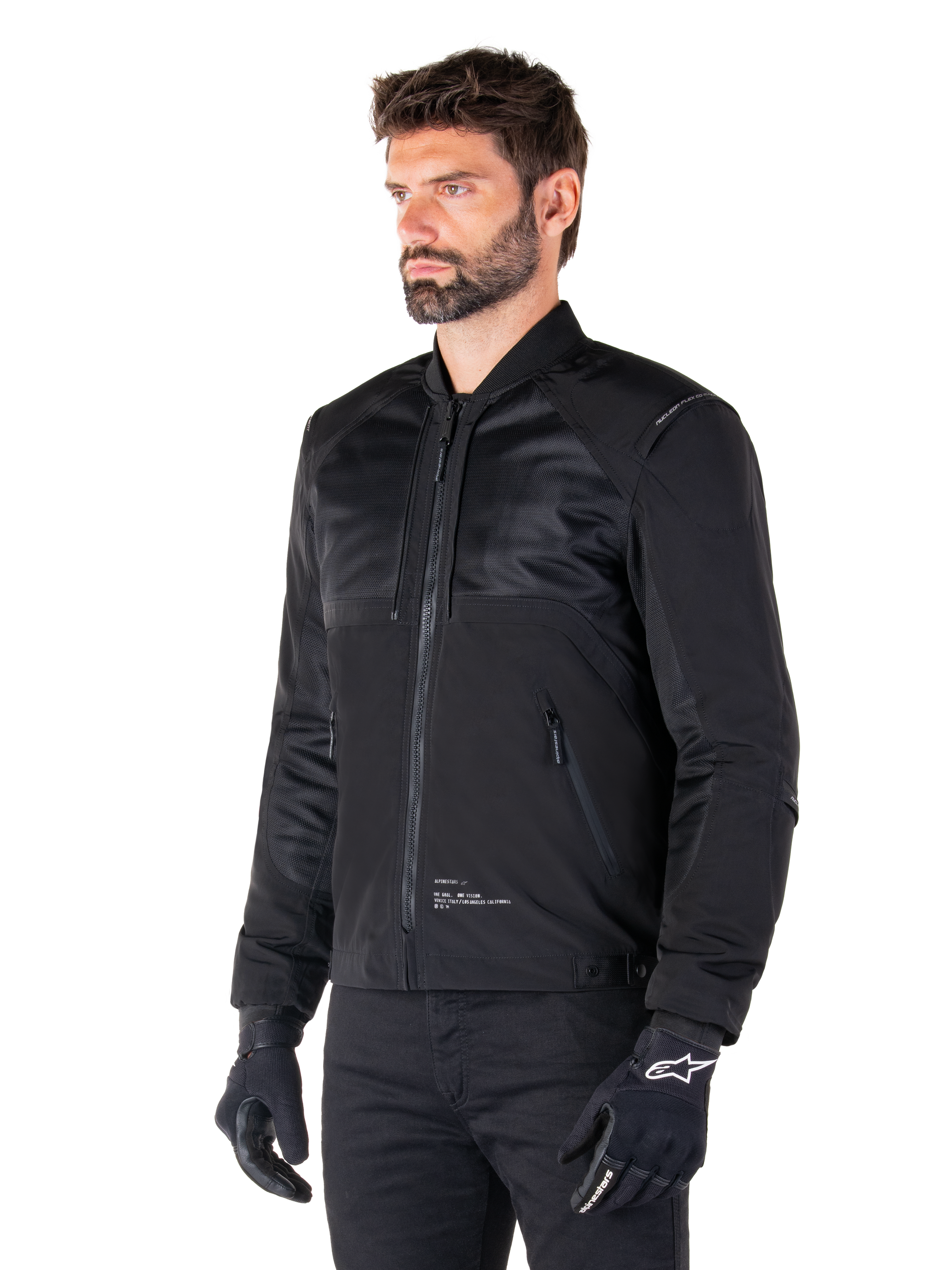 Alpinestars Mootant Waterproof Parka, modular black motorcycle jacket shown in its bomber configuration with mesh upper body panels and a ribbed collar, worn by a model with black riding gloves and pants, urban contemporary streetwear style.