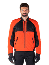 Alpinestars Mootant Waterproof Parka in Spicy Orange and Black, modular motorcycle jacket shown in a bomber-style configuration on a male model, featuring black mesh upper chest panels, bright orange torso and sleeves, front zipper, and ribbed collar, paired with black gloves and trousers