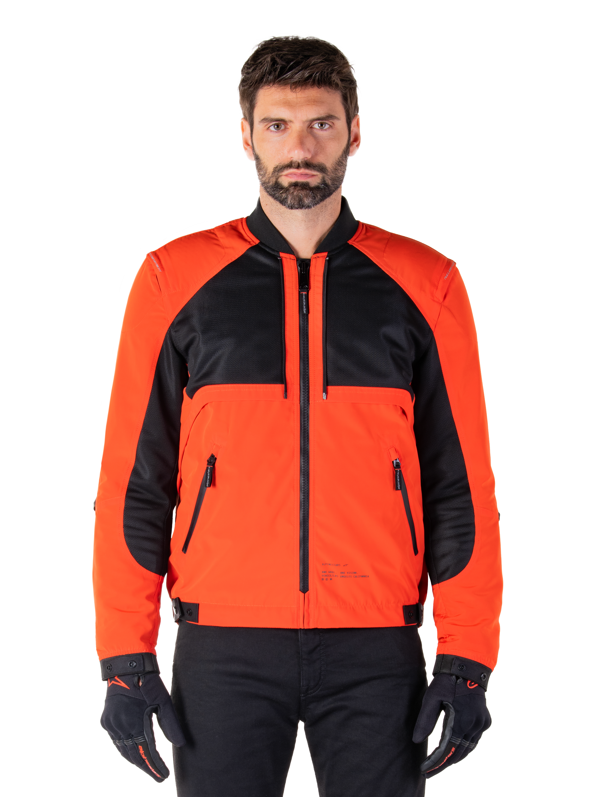 Alpinestars Mootant Waterproof Parka in Spicy Orange and Black, modular motorcycle jacket shown in a bomber-style configuration on a male model, featuring black mesh upper chest panels, bright orange torso and sleeves, front zipper, and ribbed collar, paired with black gloves and trousers