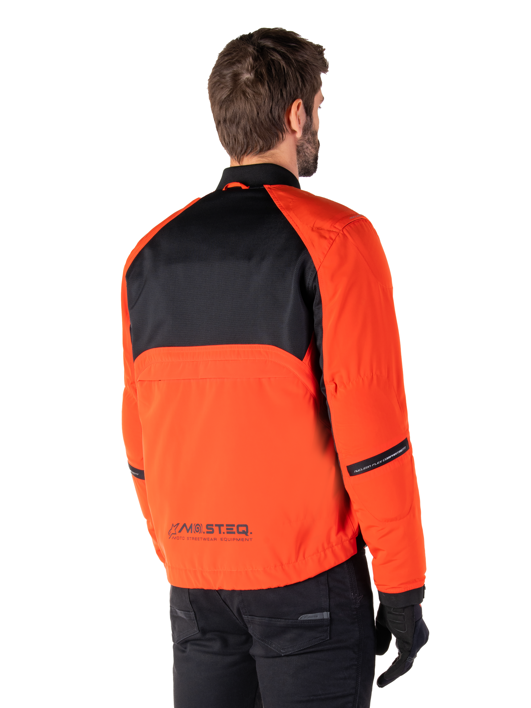 Rear view of a rider wearing the Alpinestars Mootant Waterproof Parka in Spicy Orange and Black, featuring a black mesh upper back panel and reflective MO.ST.EQ. branding, modern utilitarian motorcycle jacket.