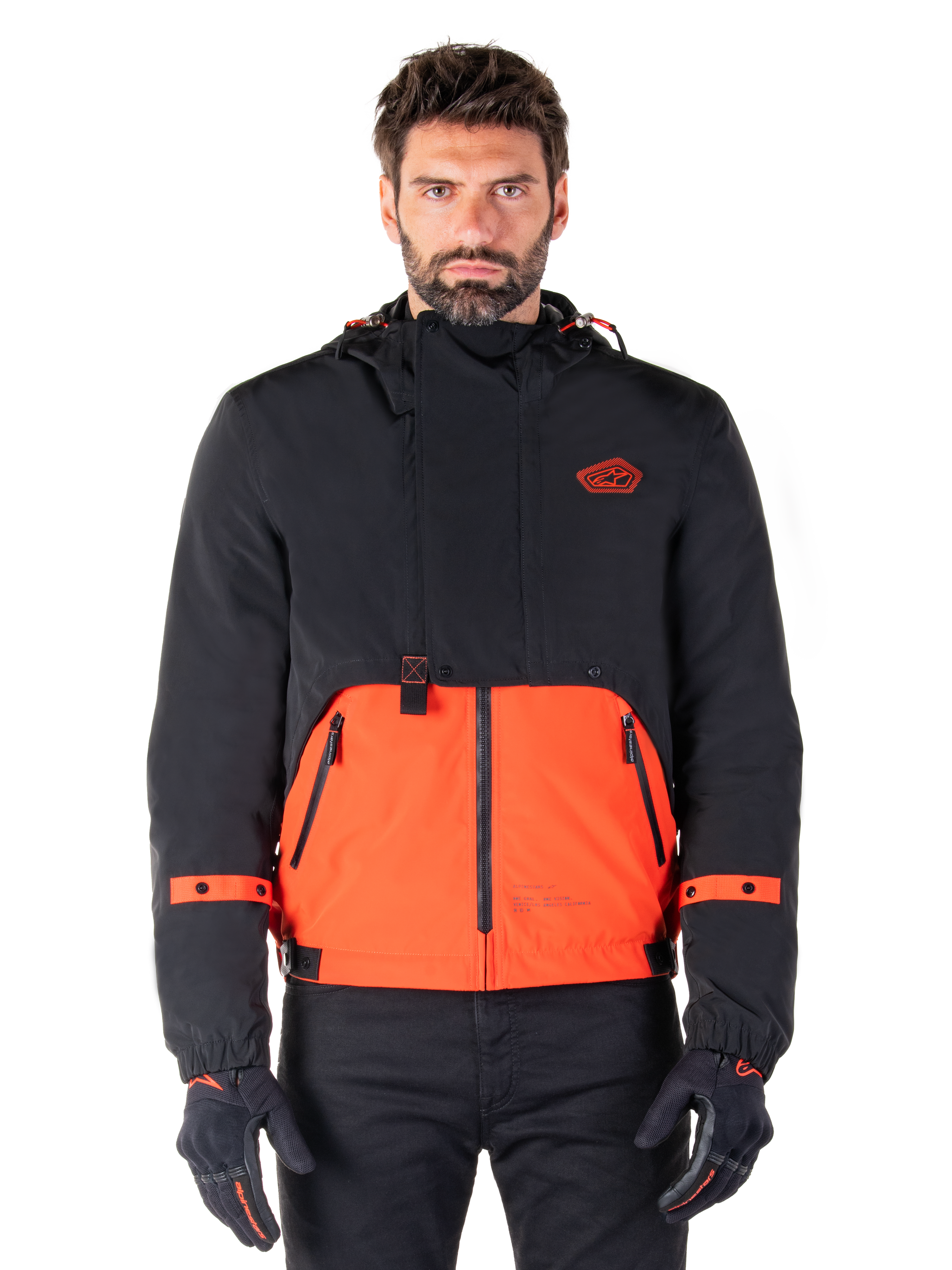 Alpinestars Mootant Waterproof Parka, modular motorcycle jacket in Spicy Orange and Black, worn by a model with matching gloves, features a hooded design with two-tone panels, front zipper, and adjustable cuffs, urban contemporary riding apparel
