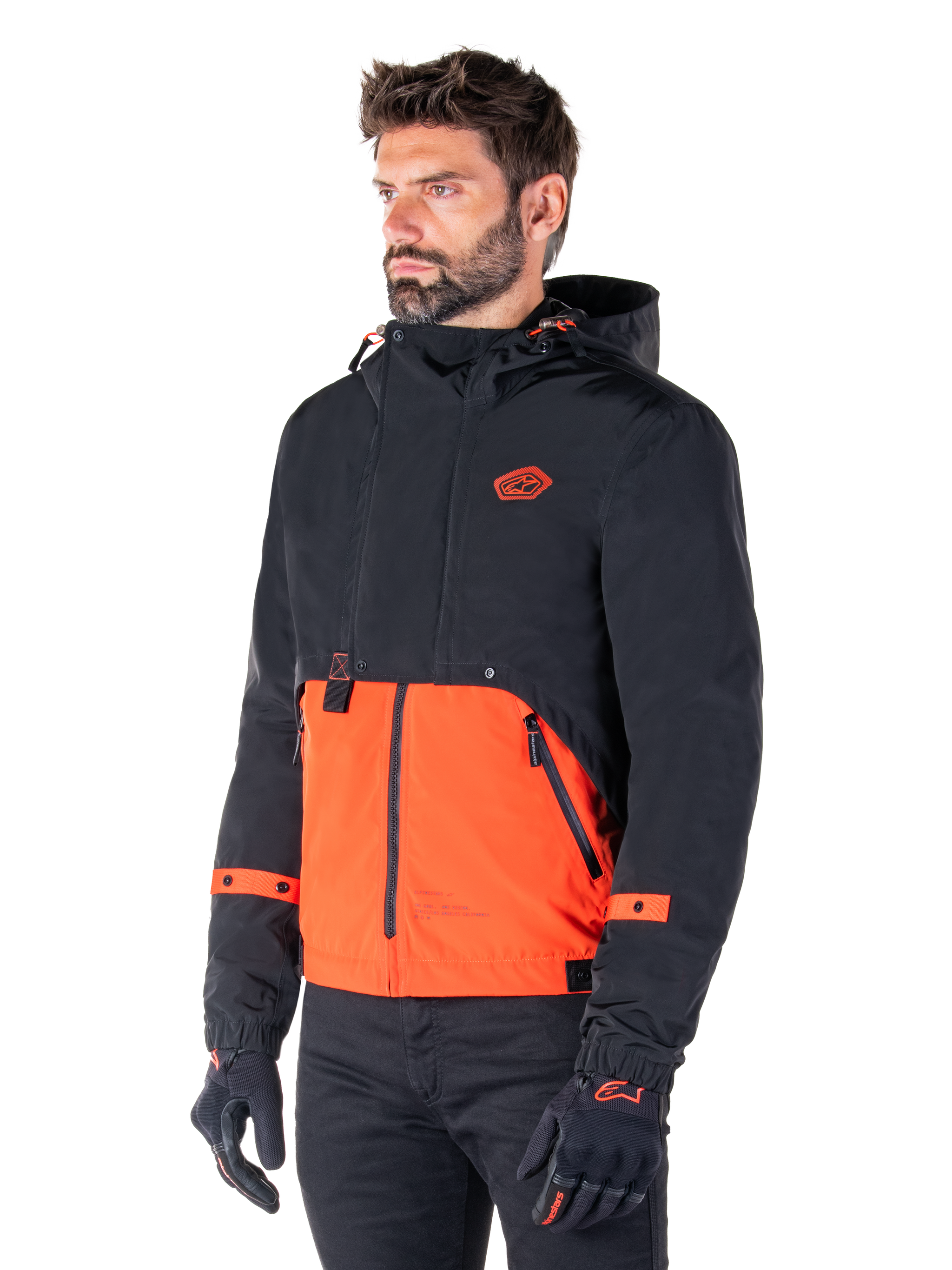 Man wearing the Alpinestars Mootant Waterproof Parka in Spicy Orange and Black, a modular motorcycle jacket with a black hooded upper layer and bright orange lower section, styled with black riding gloves and pants.