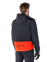 Alpinestars Mootant Waterproof Parka, Spicy Orange and Black, rear view on a male model, features a hooded black upper and bright orange lower section with MO.ST.EQ. branding, urban contemporary motorcycle jacket worn with black pants and gloves
