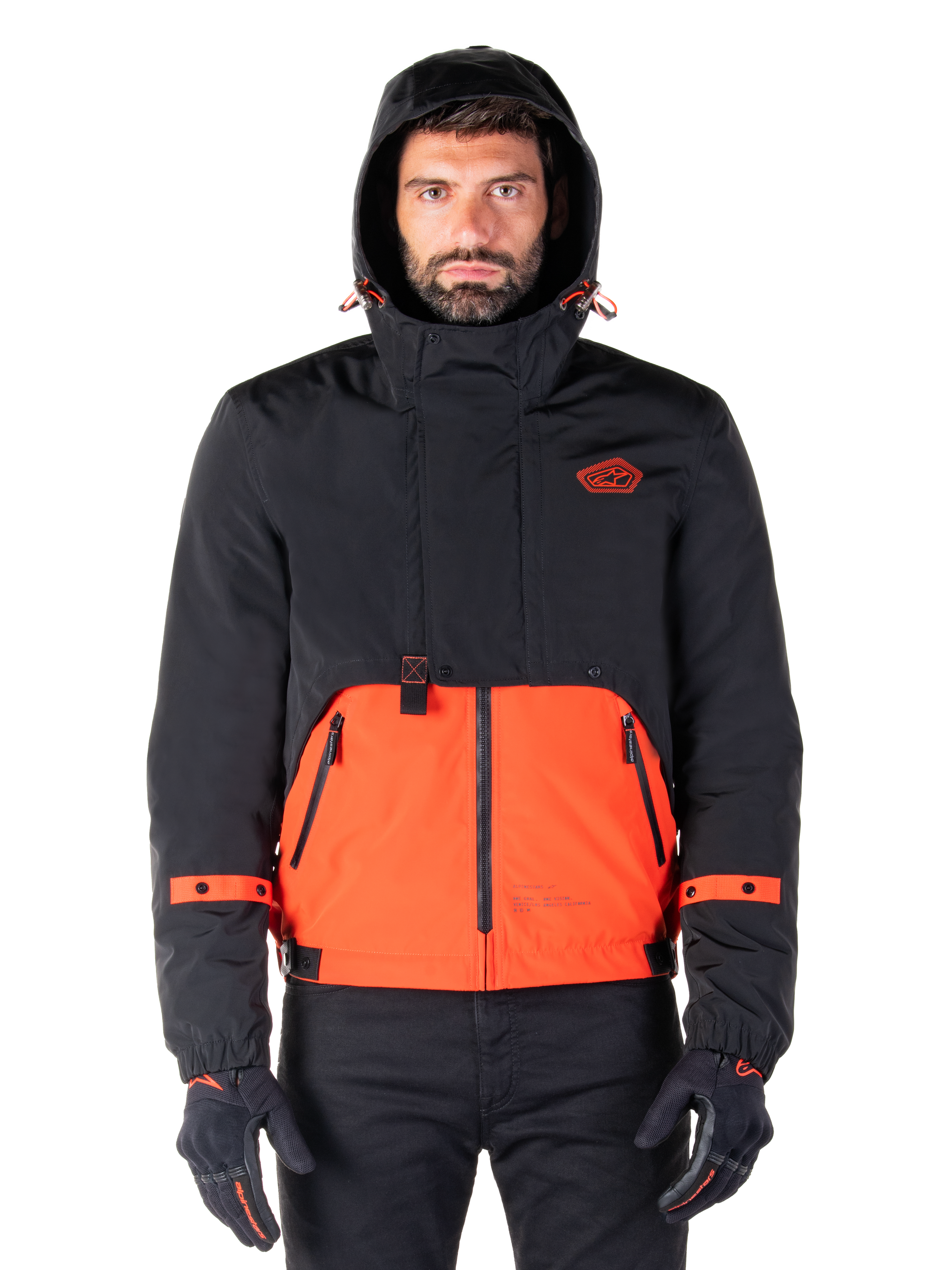 Alpinestars Mootant Waterproof Parka, Motorcycle Jacket, Spicy Orange and Black, modular all-weather design with hood, front zippered pockets, and orange strap details on sleeves, worn by a model with black gloves and pants
