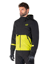 Alpinestars Mootant Waterproof Parka in Lime Punch Black, modular motorcycle jacket worn by a man with black riding gloves and pants, featuring a black upper section and sleeves with a vibrant lime green lower panel, hooded design with a utilitarian military-inspired aesthetic.
