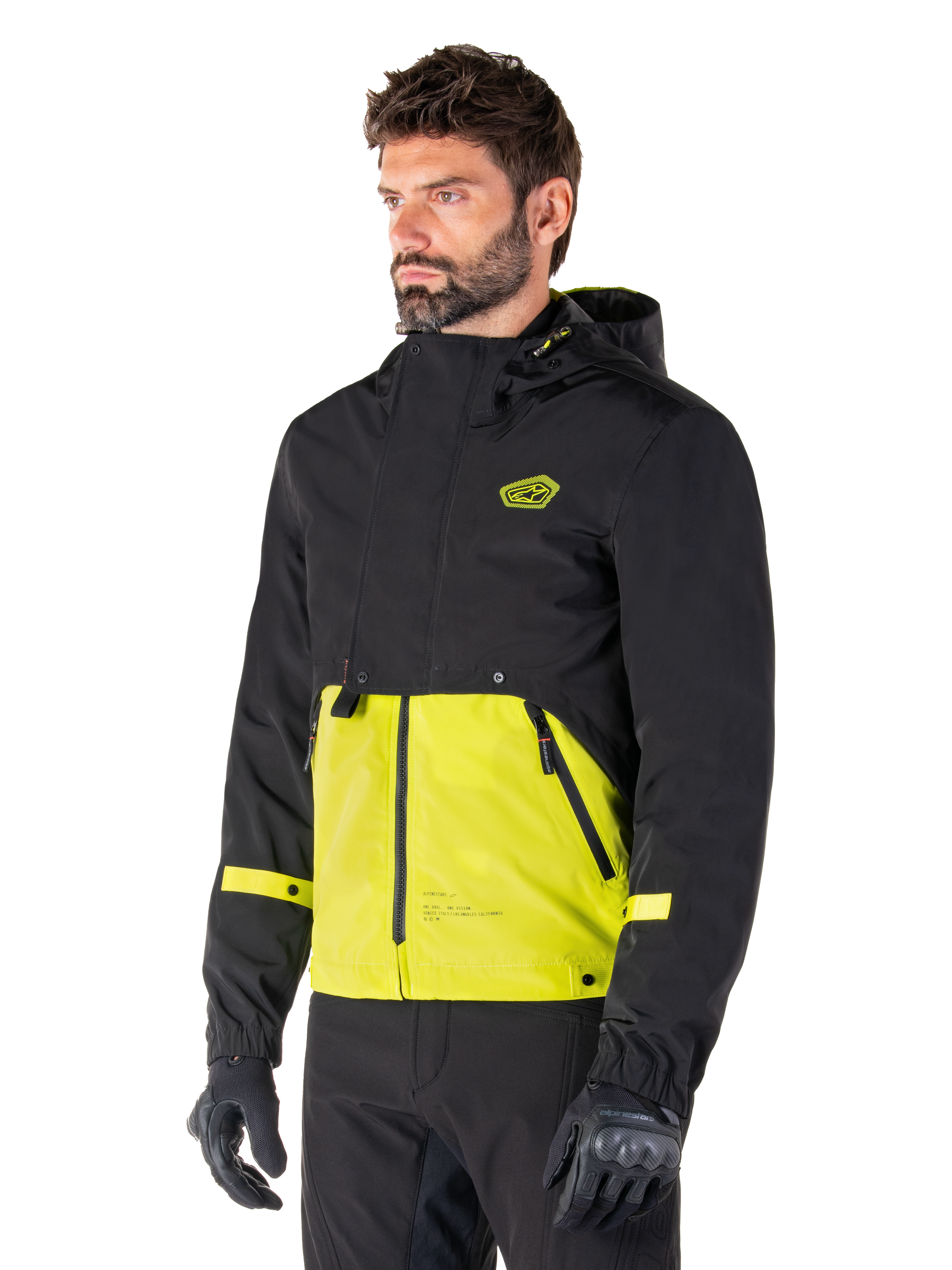 Alpinestars Mootant Waterproof Parka in Lime Punch Black, modular motorcycle jacket worn by a man with black riding gloves and pants, featuring a black upper section and sleeves with a vibrant lime green lower panel, hooded design with a utilitarian military-inspired aesthetic.