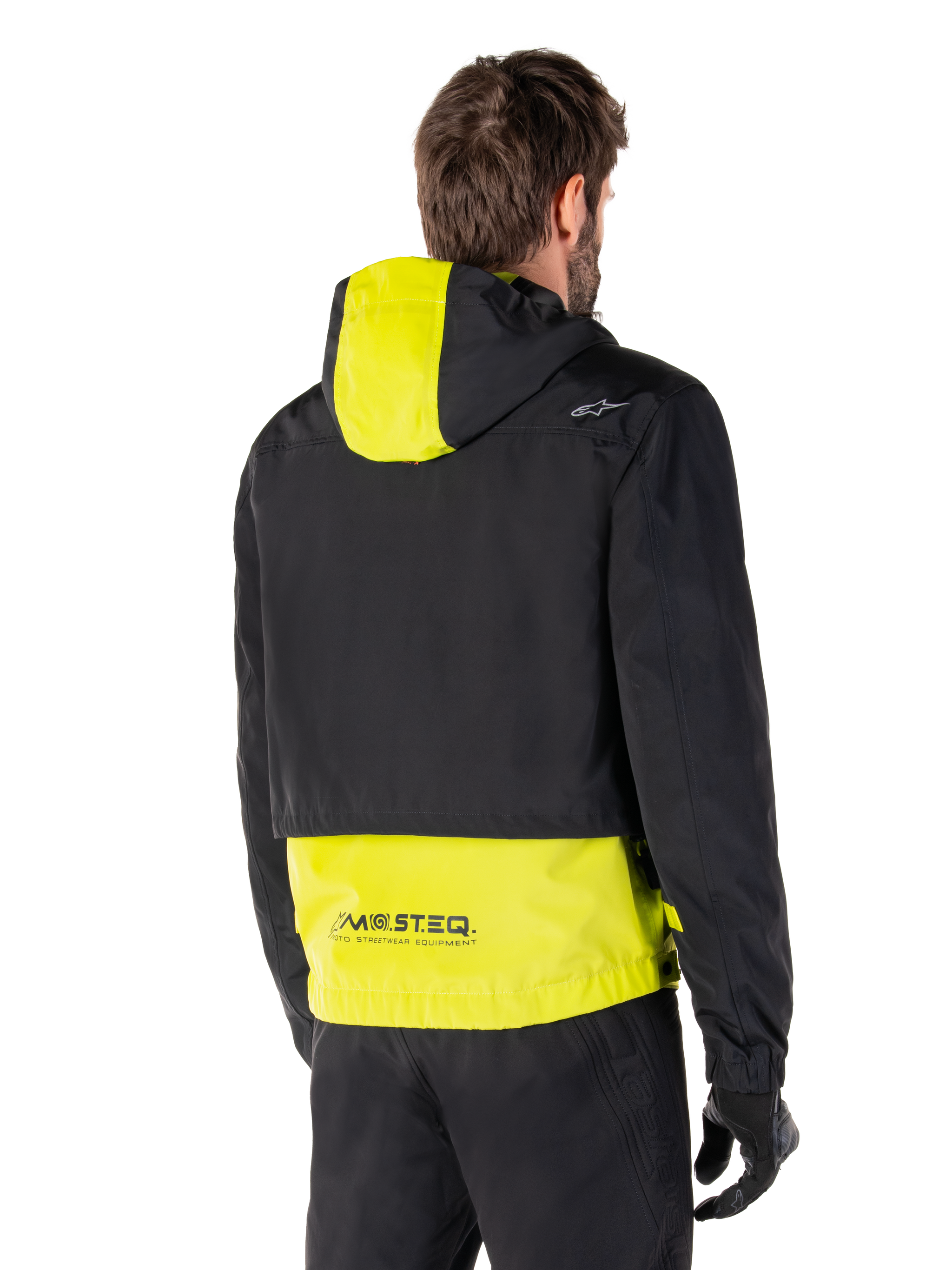 Alpinestars Mootant Waterproof Parka, Rear View, Lime Punch and Black, featuring a black upper body with a lime yellow hood panel and lower back, MO.ST.EQ. branding on the hem, worn with black riding pants and gloves, urban contemporary motorcycle jacket