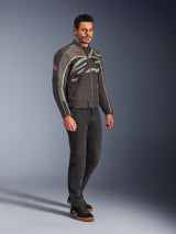 Male model wearing the Alpinestars Axton Jacket in Black Anthracite Red Tangerine, vintage-inspired motorcycle jacket with a wrap-around logo and red accents, paired with black pants and black riding sneakers, urban contemporary motorcycle gear