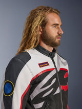 Man with long hair and beard wearing the Alpinestars Axton Jacket, Motorcycle Jacket, Black Off White and Bright Red, vintage racing-inspired design with branded patches and wrap-around logo, close-up profile view, urban contemporary style