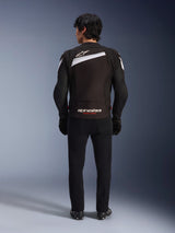 Alpinestars T-GP Plus R V4 Jacket, Black and White sport textile motorcycle jacket, rear view featuring white Alpinestars logo and 'RACING AHEAD' branding, worn with black trousers and boots, streamlined design for performance riding.