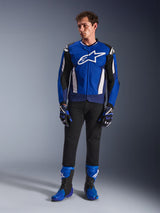 Male model wearing the Alpinestars T-GP Air Jacket in Bright Blue Navy White, paired with black pants, matching blue and navy racing gloves, and blue and black motorcycle boots, studio shot showcasing a complete sport riding outfit.