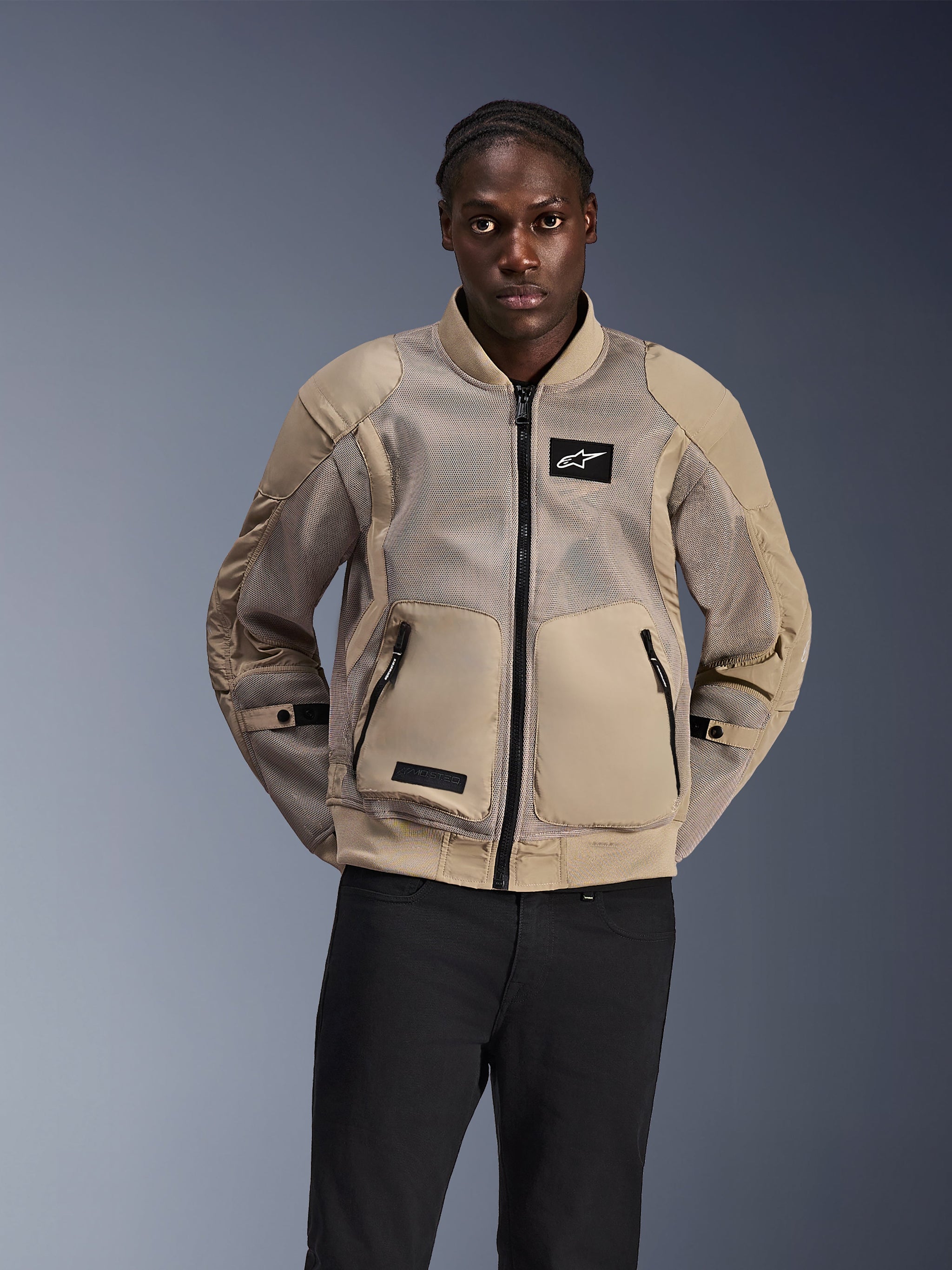 Alpinestars Flight Air Jacket, Bomber-style urban motorcycle jacket, Light Tan, featuring extended 3D mesh panels for ventilation and large front pockets, worn by a man with black pants, modern motorsport-inspired design for hot-weather riding