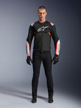 Male model wearing Alpinestars T-Sps Air V2 Jacket in Black White Red Fluo, featuring large tech mesh panels and bold white branding on the chest and sleeves, paired with black technical riding pants and gloves, urban sport motorcycle gear