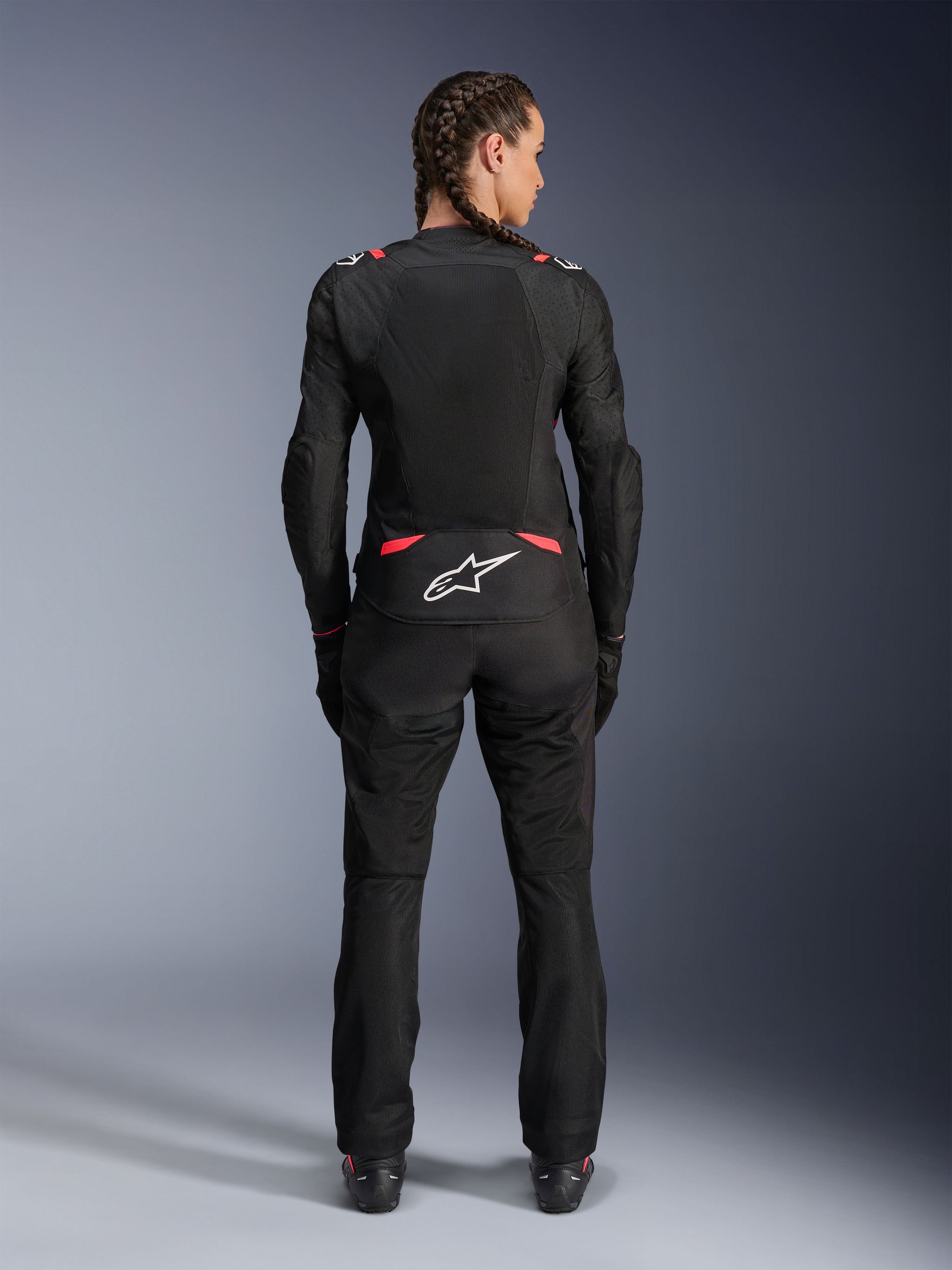 Alpinestars Stella T-SPS Air V2 Jacket, Women's Textile Motorcycle Jacket, Black and Diva Pink, rear view on model with braided hair, featuring large mesh panels for ventilation, white Astars logo on the lower back, paired with matching black riding pants.