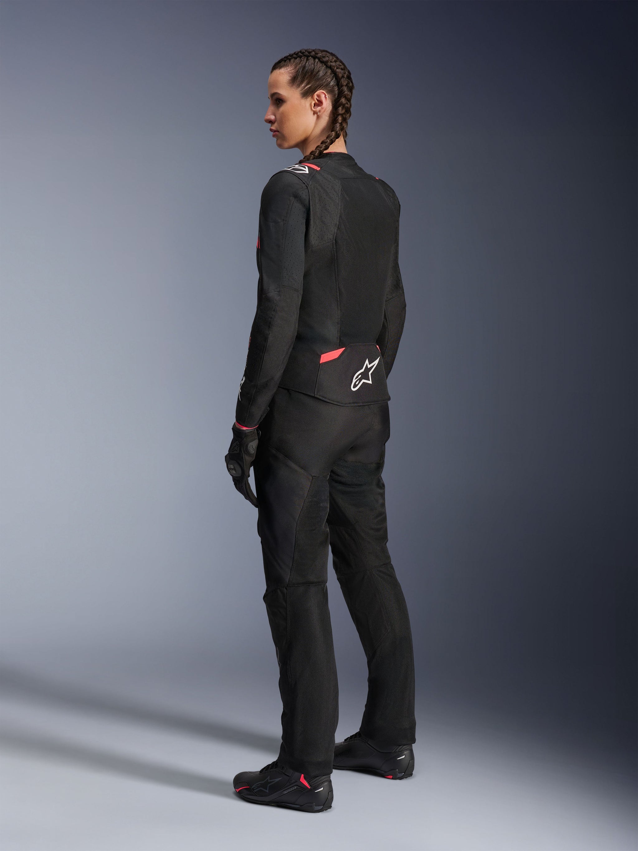 Alpinestars Woman Stella T-Sps Air v2 Jacket, Black and Diva Pink, textile motorcycle jacket shown from a rear-side view, featuring large mesh panels for airflow and white star logo on the back, worn with matching black riding pants, gloves, and boots.