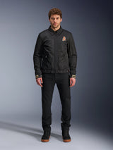 Male model wearing the Alpinestars Ignite Air Jacket in black, featuring a classic shirt collar, full front zipper, and an orange logo on the chest. Styled with black pants and black high-top sneakers for an urban contemporary motorcycle look.