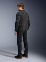 Alpinestars Ignite Air Jacket, Black motorcycle jacket, rear view featuring white graphic text on the upper back and tan striped cuffs, Harrington-style silhouette with mesh body, paired with black pants and black sneakers