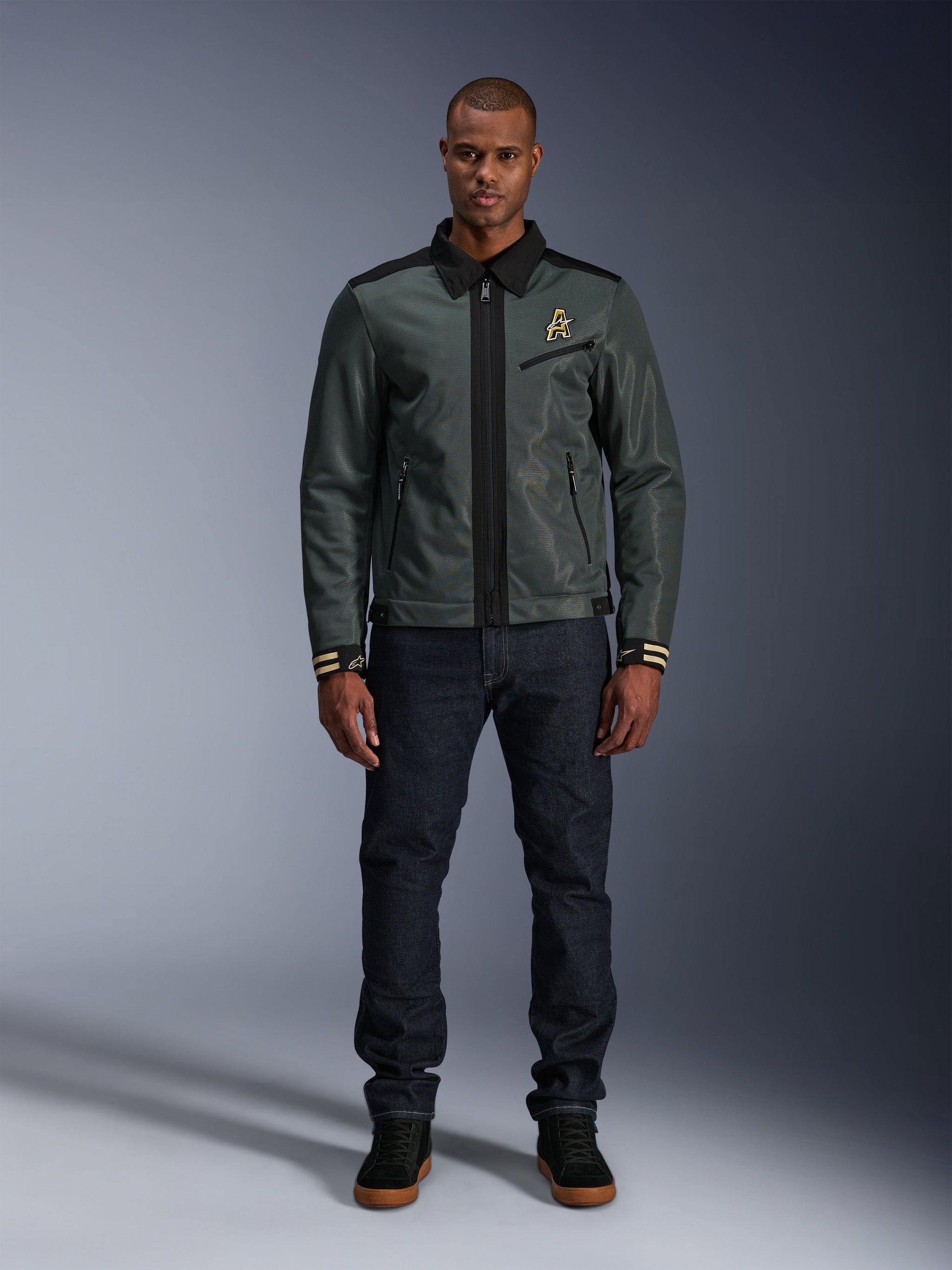 Alpinestars Ignite Air Jacket in Urban Gray Black Blue, Harrington-style motorcycle jacket with shirt collar and mesh construction, worn by a man with dark denim jeans and black sneakers, urban streetwear for riders.
