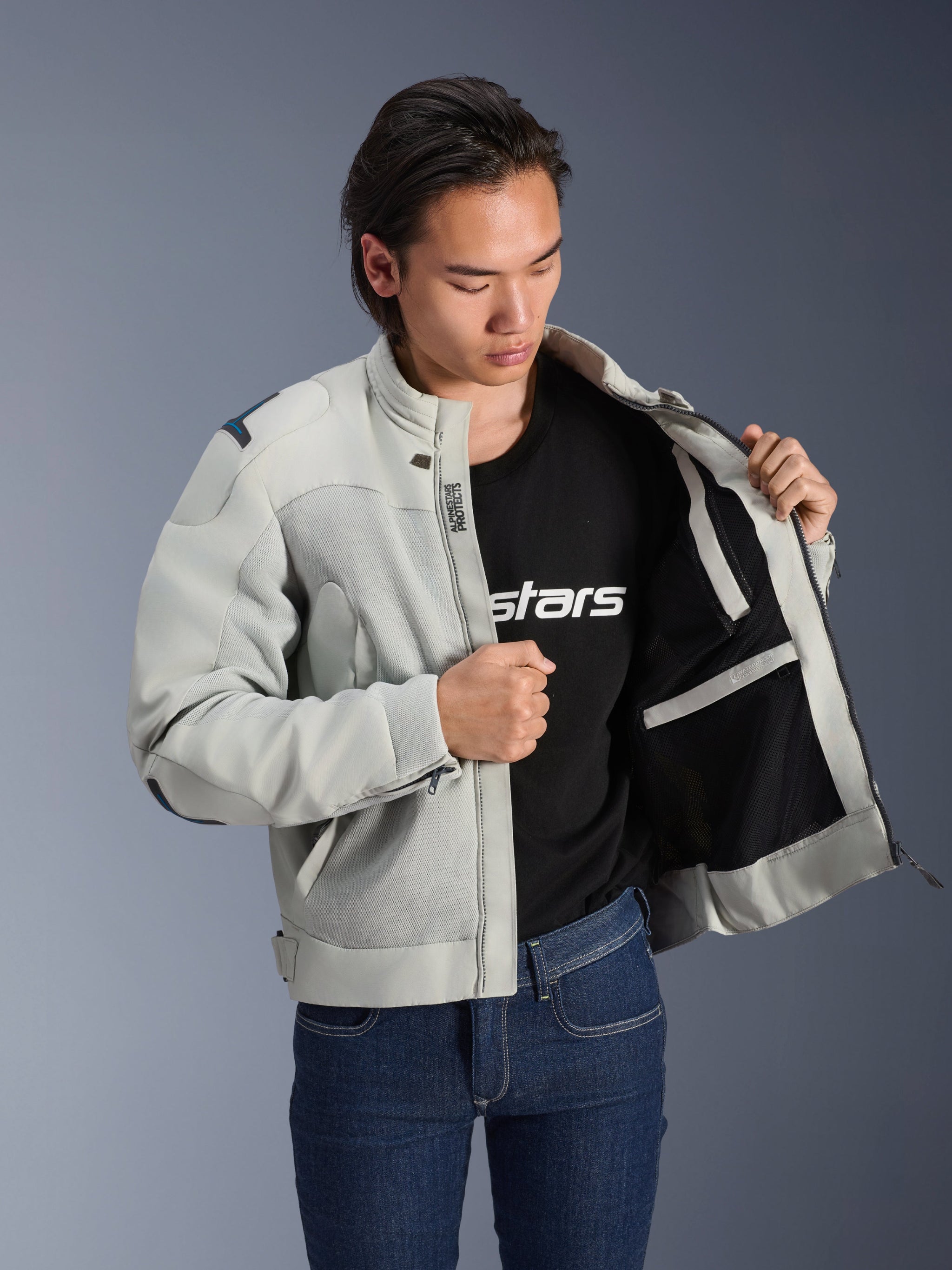 Alpinestars Circal-1 Air Jacket, Metal Gray, held open to show interior mesh lining and pocket details, worn by a model with a black logo t-shirt and blue jeans, urban motorcycle style