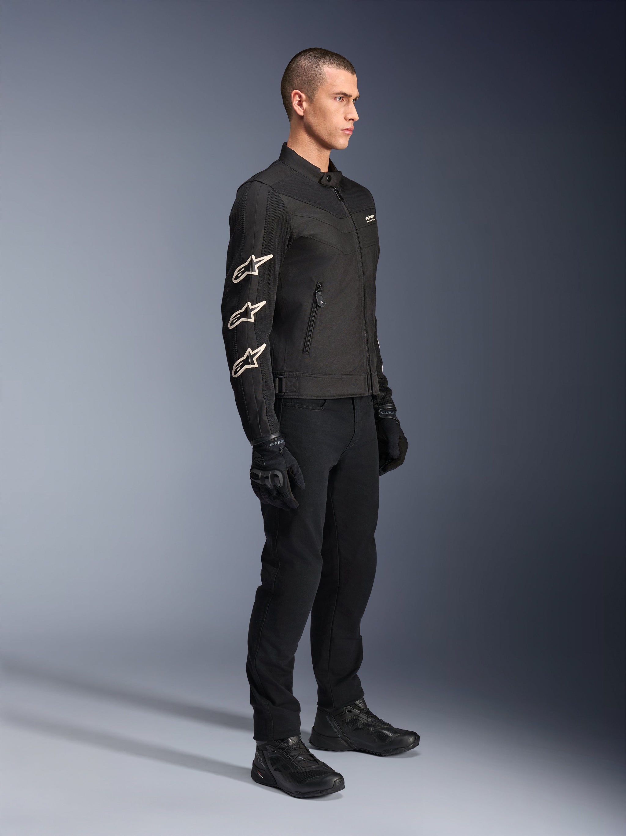 Alpinestars T-Dyno Air Jacket, Black, textile motorcycle jacket, featuring three white Alpinestars logos on the sleeve, worn with matching black pants and gloves, urban riding gear with breathable mesh panels