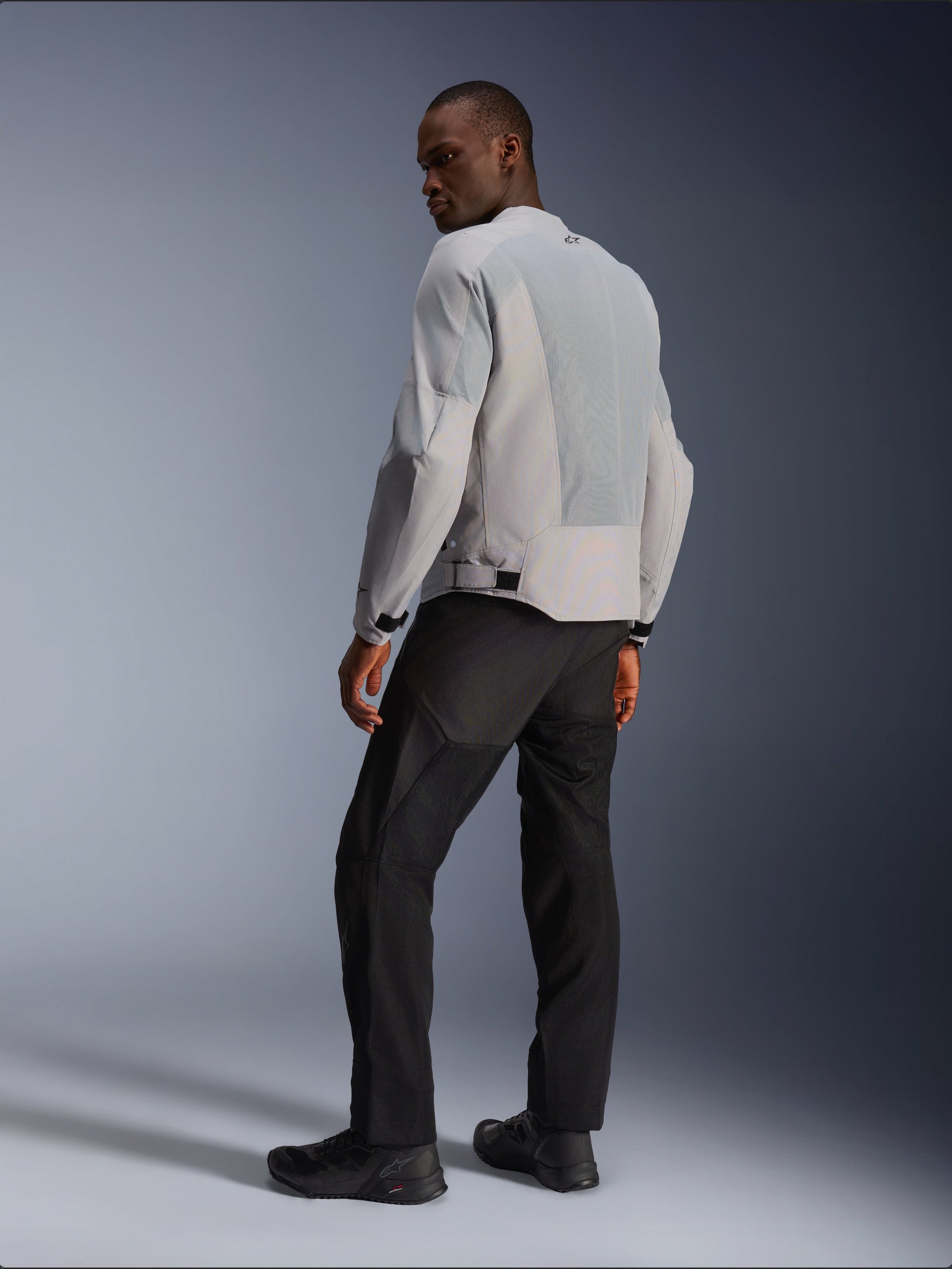 Alpinestars C-1 Air Jacket, Silver and Gray, viewed from the back on a model, featuring ventilated tech mesh panels and reflective logos, worn with black pants and shoes, urban contemporary motorcycle riding gear.