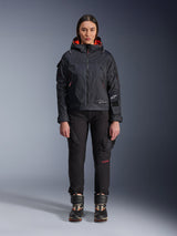 Female model wearing the Alpinestars Molly Air Jacket in Black and Fluo Coral, featuring a utility-inspired design with a hood and coral inner lining, paired with black riding pants and motorcycle boots, urban contemporary motorcycle gear