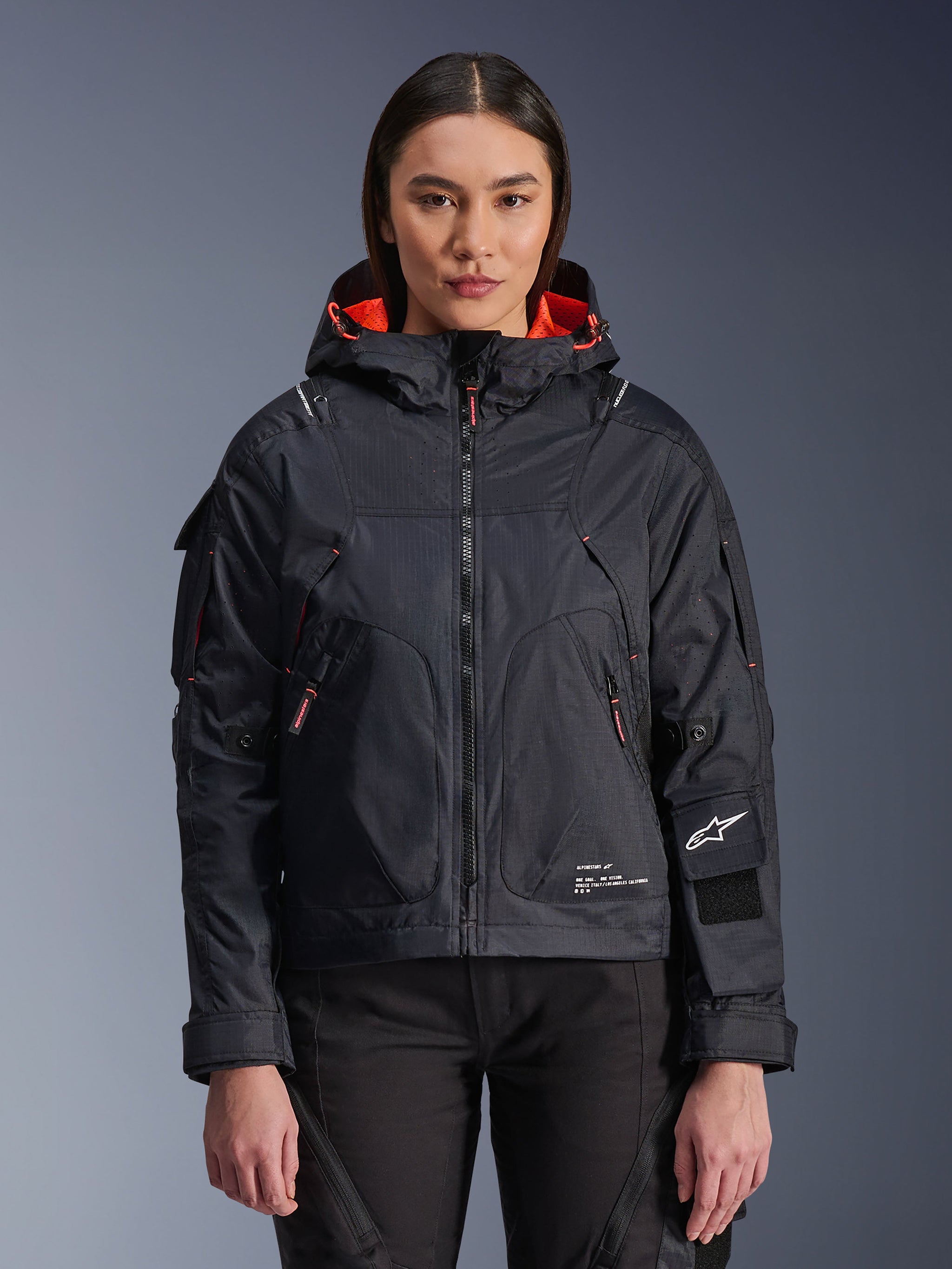 Alpinestars Molly Air Jacket, Women's Motorcycle Urban Jacket, Black with Fluo Coral interior lining, worn by a female model, hooded design with technical textile construction, zippered pockets and Alpinestars logo on the sleeve