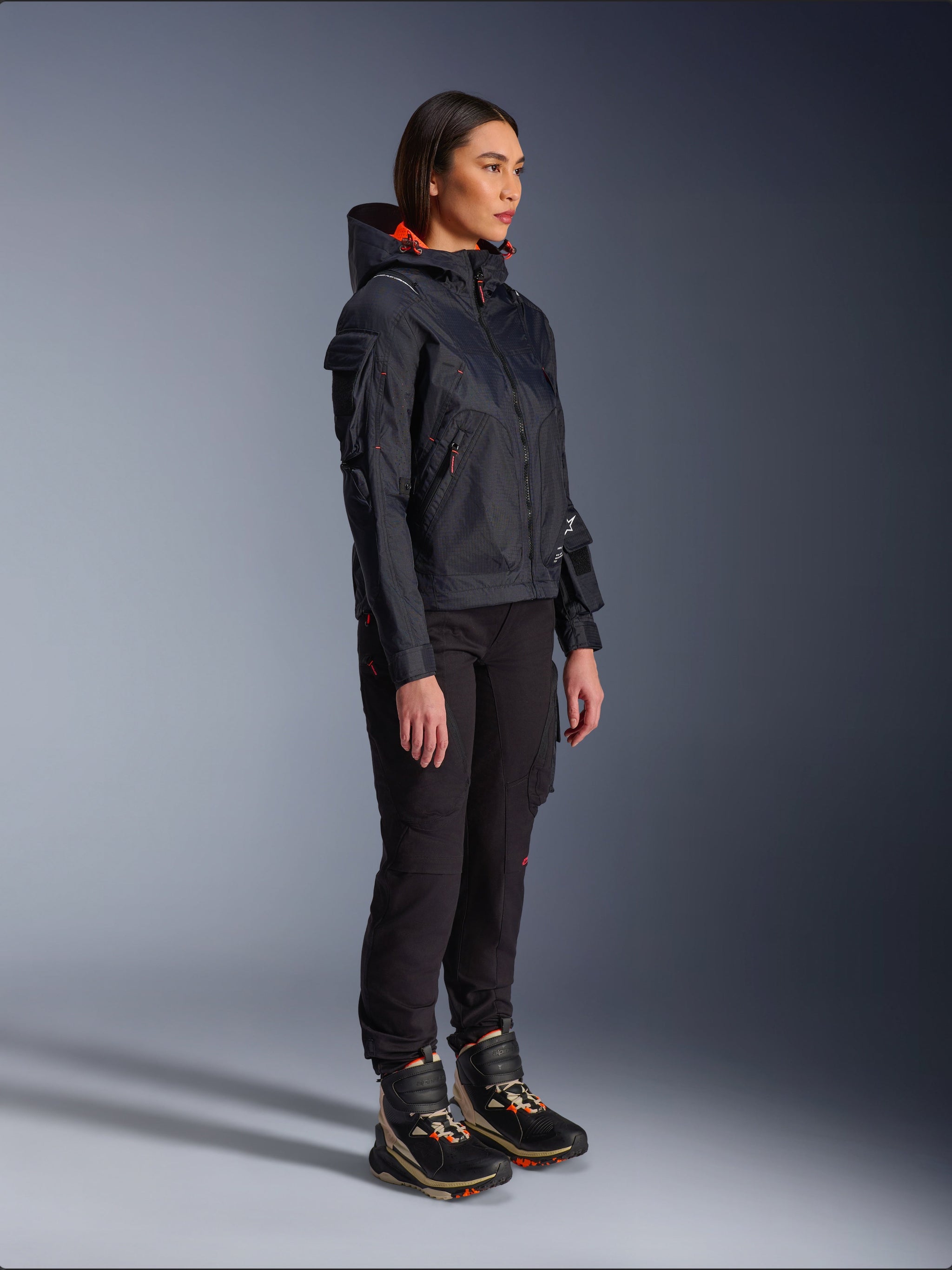 Alpinestars Actea Women's Pants in Black, regular fit with cargo pockets, styled with a black Molly Air Jacket with orange accents and high-top riding shoes, contemporary urban motorcycle apparel for women