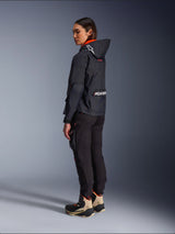 Alpinestars Actea Women's Pants, Black, modern motorcycle pants with a tapered fit and thigh cargo pocket, shown from a side-rear perspective on a model wearing a dark hooded jacket and riding boots, urban riding style.
