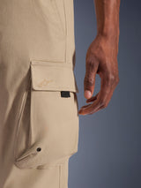 Alpinestars Flex-AST Cargo Pants, Urban Motorcycle Pants, Light Beige, close-up detail of side cargo pocket with tone-on-tone embroidered logo, metal eyelet, and black accent tab, showing durable stretch textile fabric.