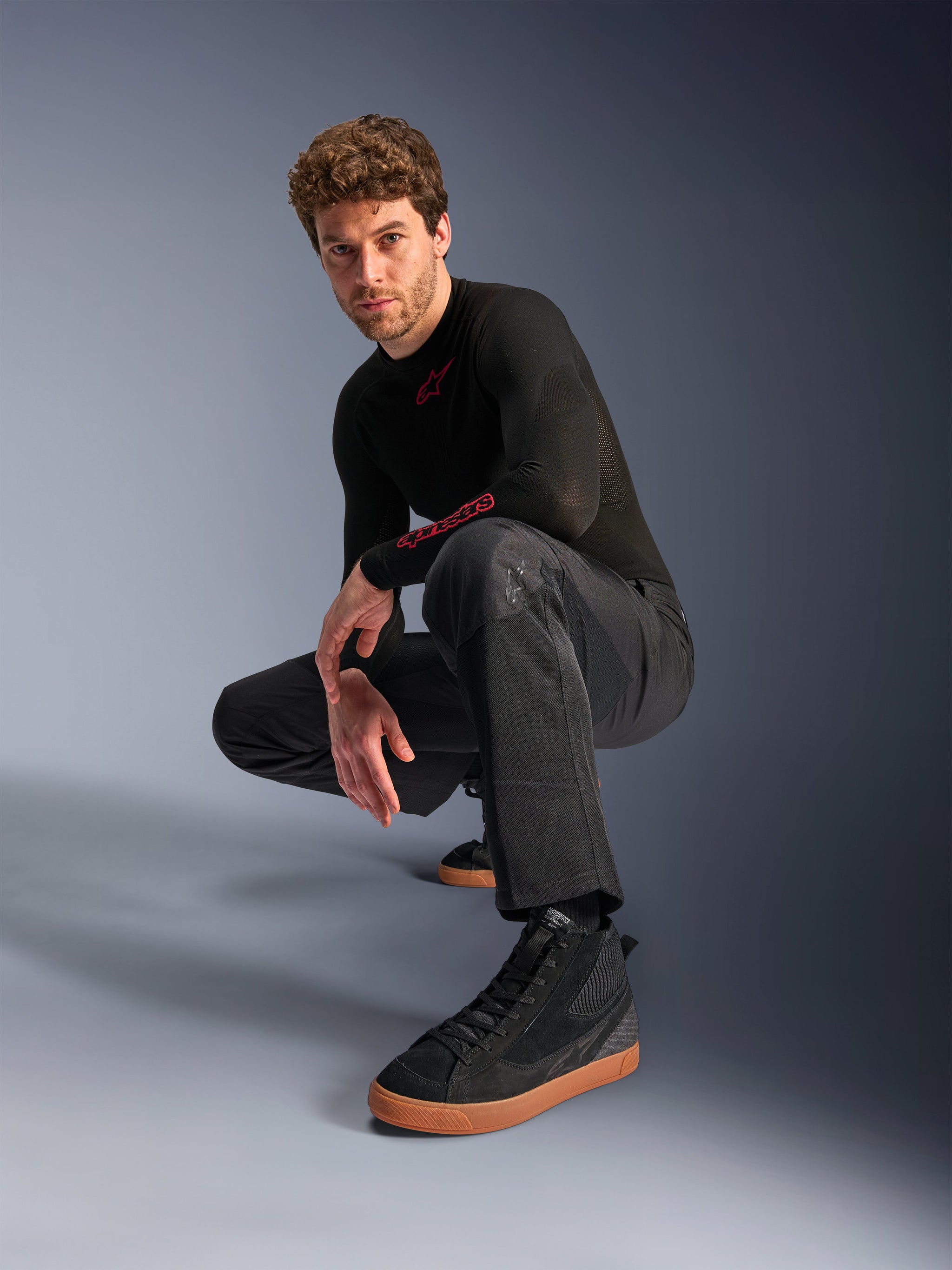 Alpinestars C-1 Air Pants, Urban Motorcycle Pants, Black, model crouching in a studio setting, worn with a black long-sleeve top and black sneakers with tan soles, featuring breathable mesh panels and a contemporary urban style