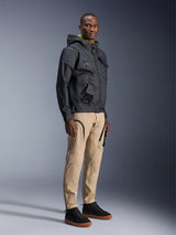 Alpinestars Acteon Pants, urban motorcycle pants, Sand color, worn by model with a dark technical jacket and black sneakers, featuring a tapered fit with black zipper accents and cargo pockets, contemporary motorsport-inspired design