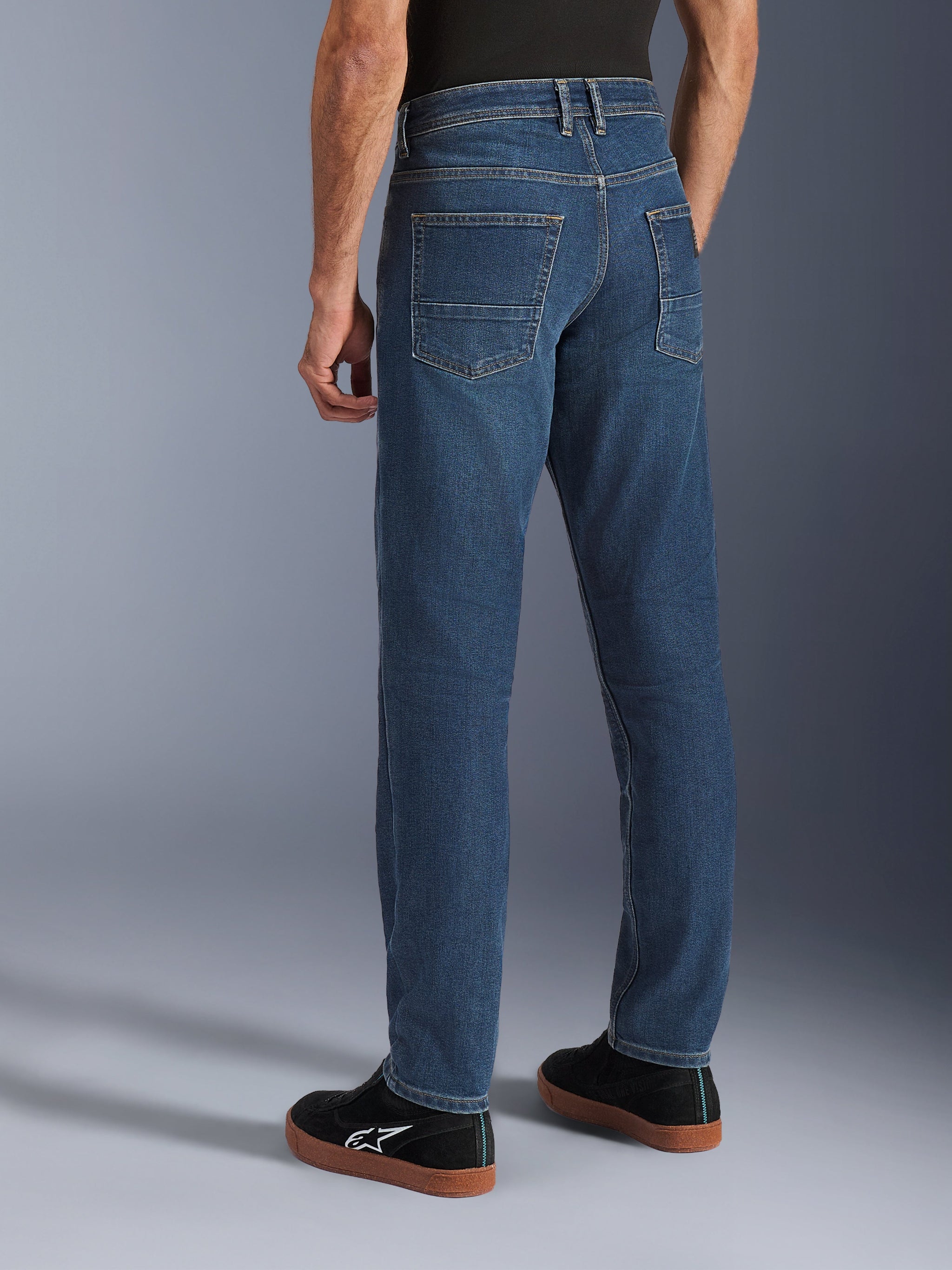 Alpinestars Flex-AST 5 Denim Pants, Indigo Washed blue, rear view of person wearing casual motorcycle jeans with a tapered fit, styled with black Alpinestars sneakers, featuring back pockets and reinforced stitching for urban riding
