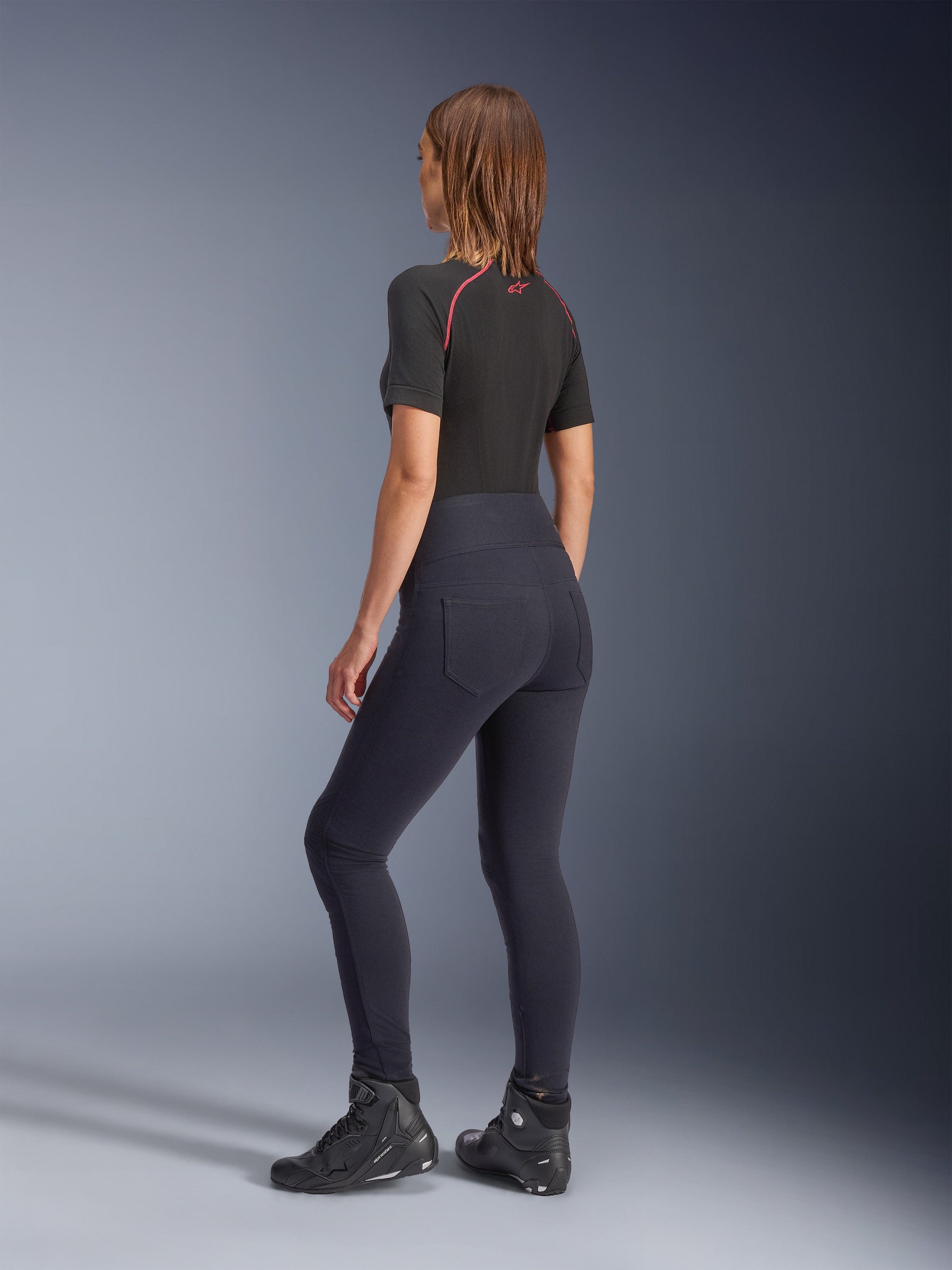 Alpinestars Woman Stella Flex-AST Leggings, black high-waisted motorcycle leggings, back view showing skinny fit and back pockets, worn with black short-sleeve top and motorcycle boots, urban riding gear for women.