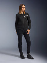 Woman wearing Alpinestars Daisy V3 Women's Riding Denim, slim-fit motorcycle pants in Rinse Black, styled with a black zip-up hoodie and riding boots, urban casual protective gear