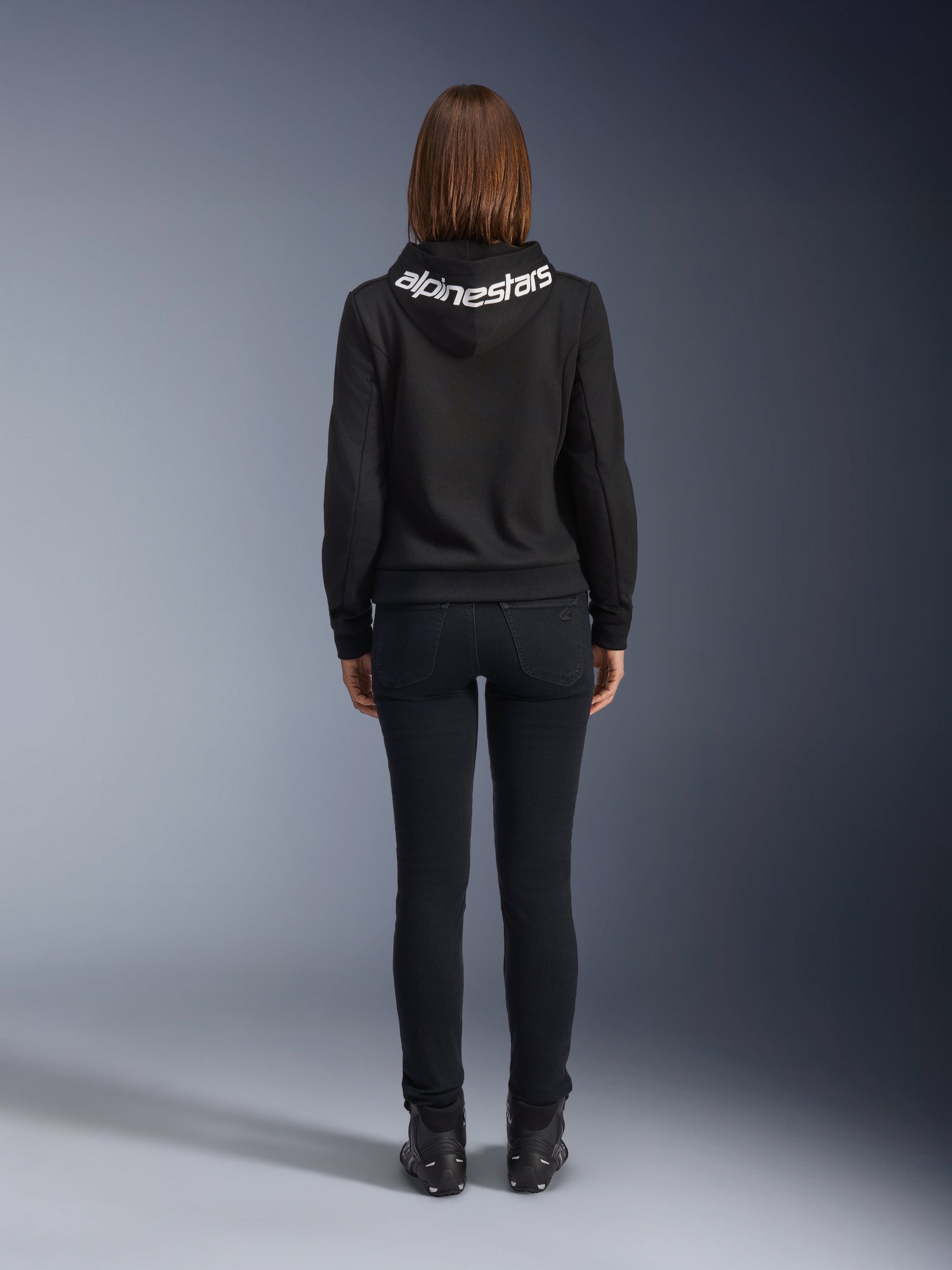 Daisy V3 Women's Riding Denim, Black Rinse, slim fit motorcycle pants, rear view showing high back waist and feminine silhouette, paired with a black Alpinestars hoodie and black riding boots, urban casual riding gear