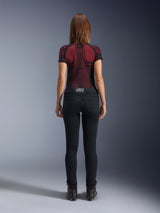 Alpinestars Daisy V3 Women's Riding Denim, Rinse Black, slim fit motorcycle pants shown from behind, featuring a high-waist design and back pockets, paired with a red and black patterned technical shirt and black boots, urban motorcycle gear for women