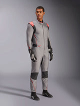 Male model wearing the Alpinestars Hypertech V3 Suit in Mid Gray with Black and Red Fluo accents, professional auto racing suit paired with black racing gloves and shoes, featuring a lightweight two-layer Nomex construction with red shoulder detailing and an athletic fit