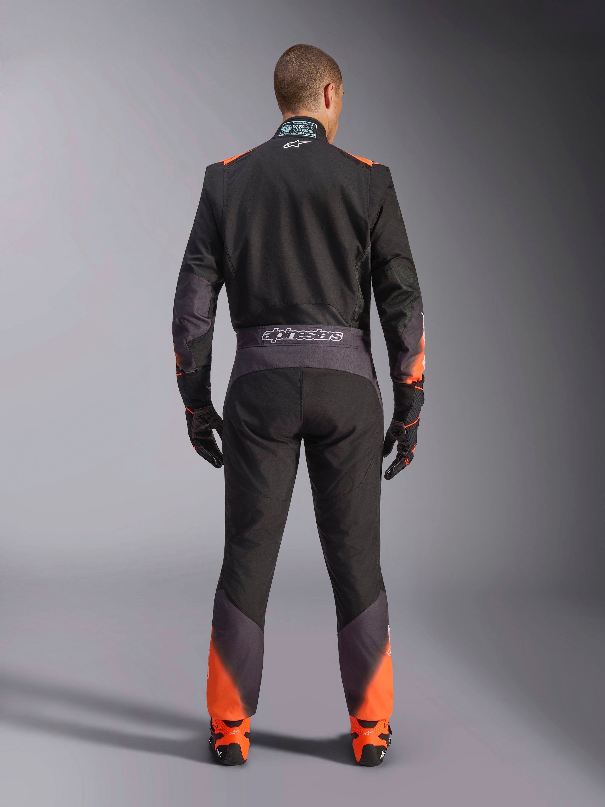 Alpinestars KMX-5 V3 Suit, men's black and orange fluo one-piece karting suit, FIA certified, rear view showing branding.