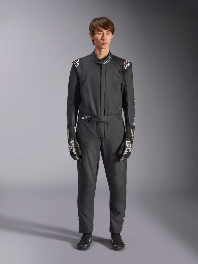 Alpinestars GP Tech V4 Suit, Black and White, professional one-piece auto racing suit, worn with matching black and white gloves and racing shoes, featuring white Alpinestars logos on shoulders and collar, sleek athletic fit for motorsport competition